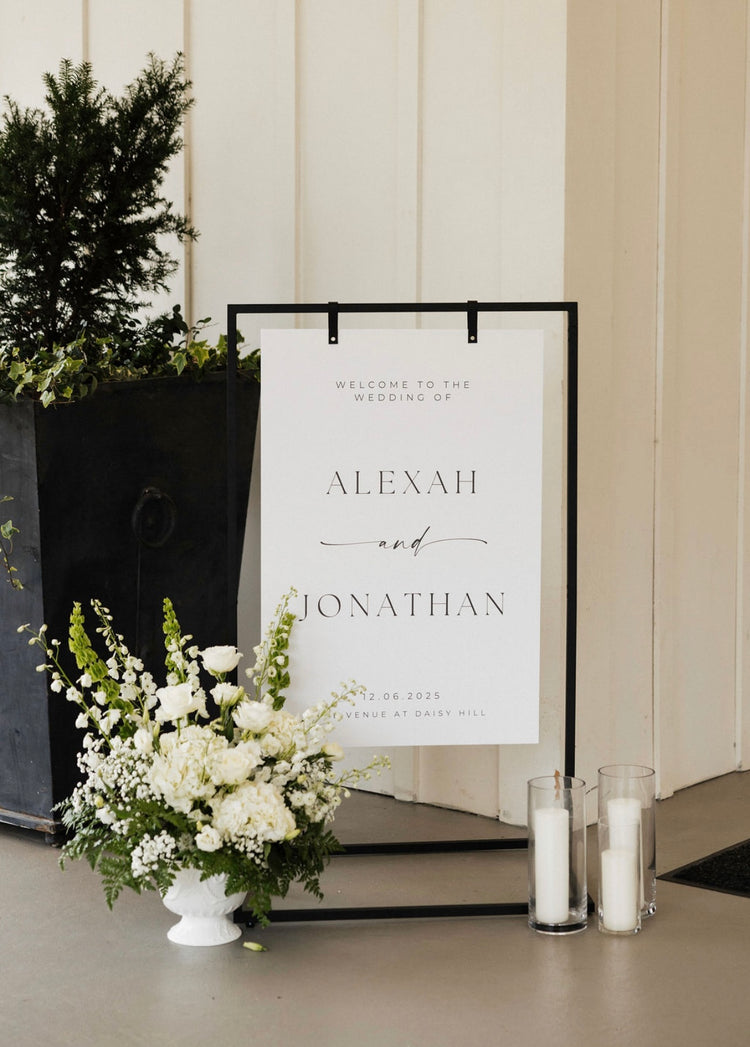 White garden-style arrangement in a pedestal urn beside a wedding welcome sign