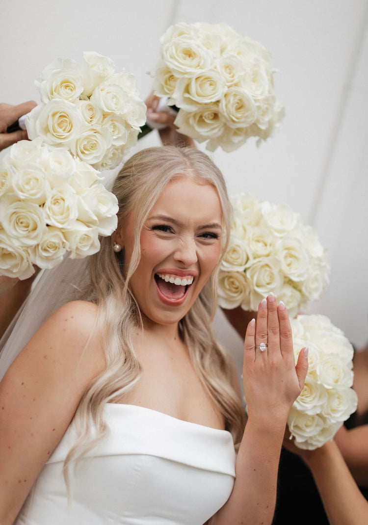 Laughing bride surrounded by bridesmaids holding white rose bouquets