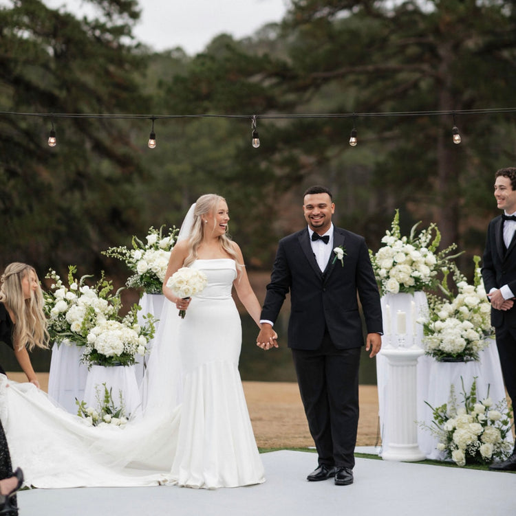 Bride and groom walking out past all-white ceremony arrangements