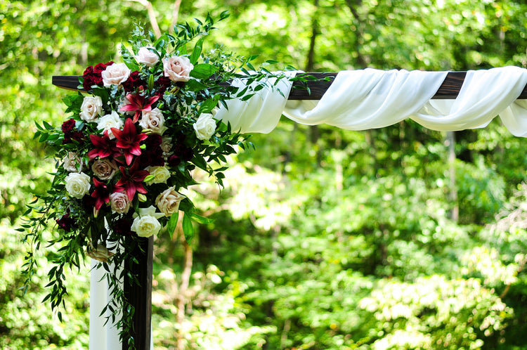 Corner arch arrangement of burgundy lilies, blush roses, and trailing greenery
