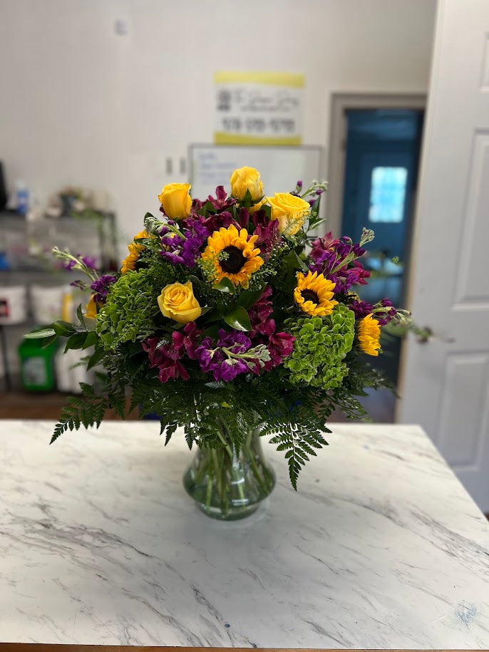 Tall arrangement of peach roses, white calla lilies, lavender stock, and blue delphinium