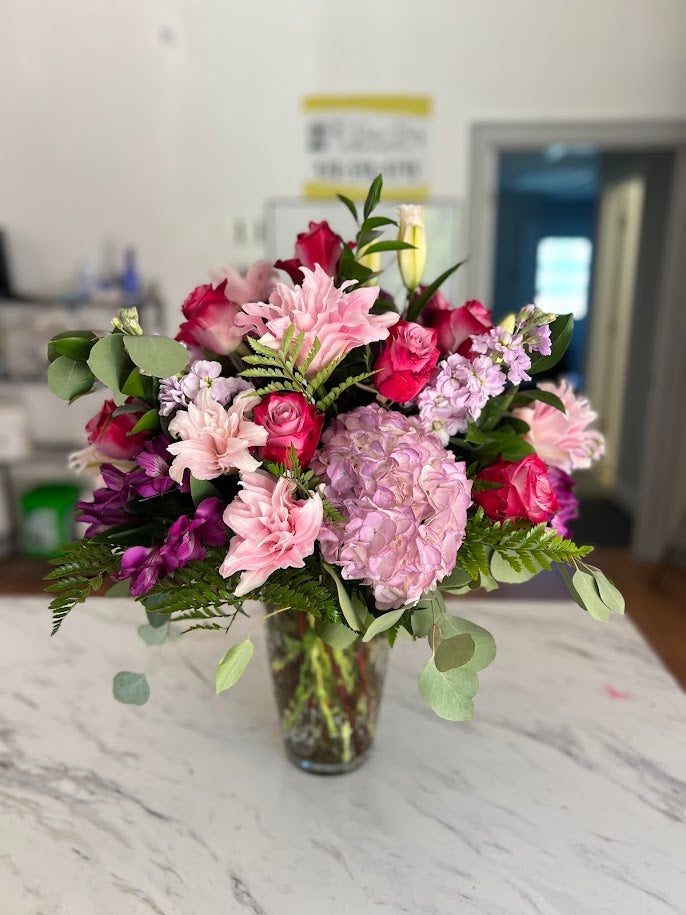 Lavender roses, a magenta gerbera daisy, and white hydrangea in a vase