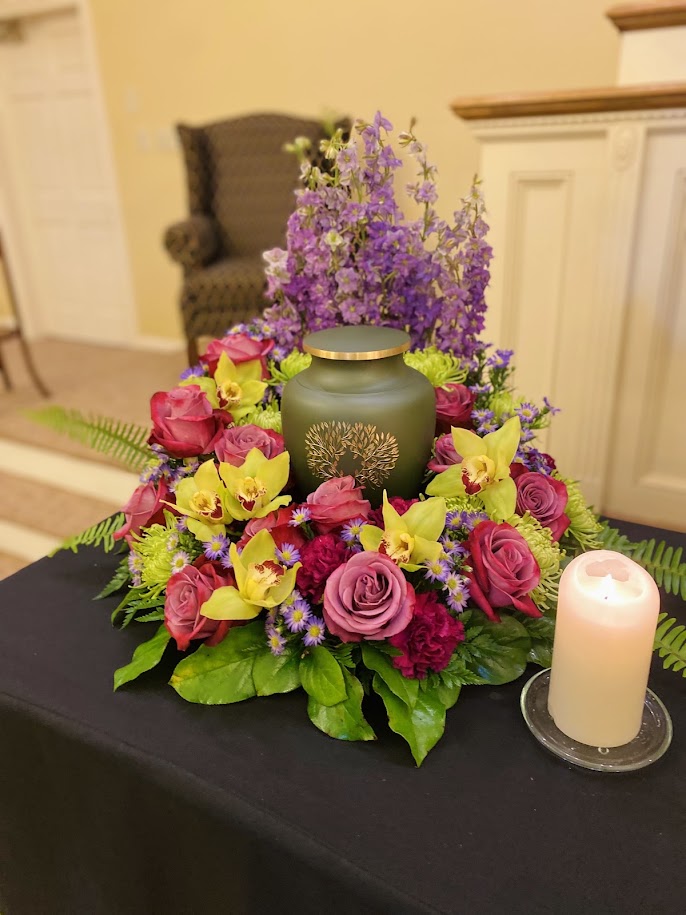 Urn surrounded by mauve roses, green cymbidium orchids, and purple delphinium