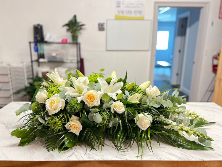 All-white casket spray of roses, lilies, and eucalyptus