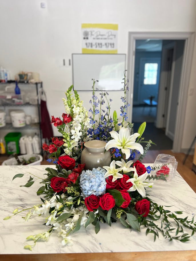 Urn arrangement of red roses, white lilies, and light blue hydrangea