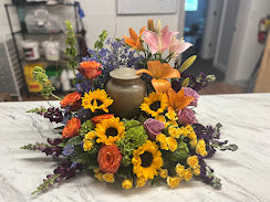 Urn surrounded by sunflowers, orange roses, and lilies