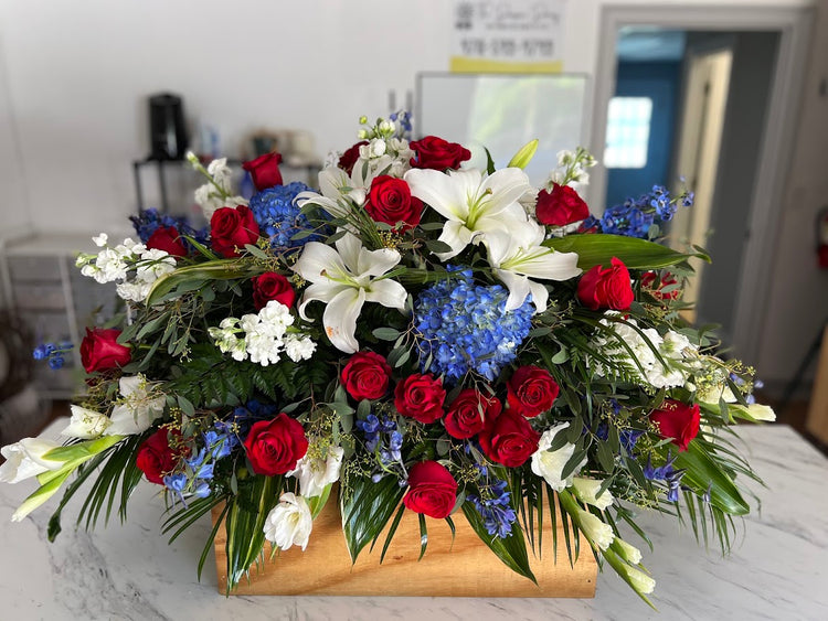Red, white, and blue casket spray of roses, lilies, and hydrangea